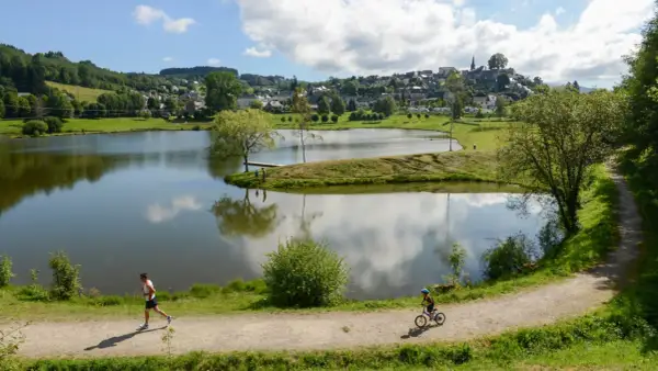 Un homme court sur le sentier, un enfant fait du vélo près du lac tour d'auvergne. Village en arrière-plan.