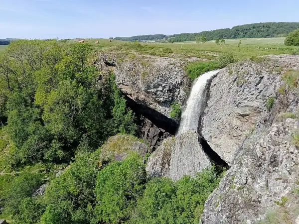 La cascade du Deroc, un lieu idéal pour la baignade, dévale une falaise rocheuse entourée de verdure.