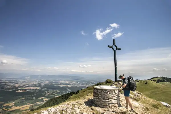 Fin d'une randonnée boucle 5 jours Jura. Un randonneur admire le panorama depuis un sommet, près d'une croix et d'un repère.