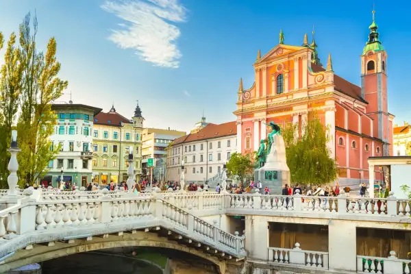 Pont triple de Ljubljana, un incontournable Slovénie, avec l'église franciscaine rose et des passants profitant du soleil.