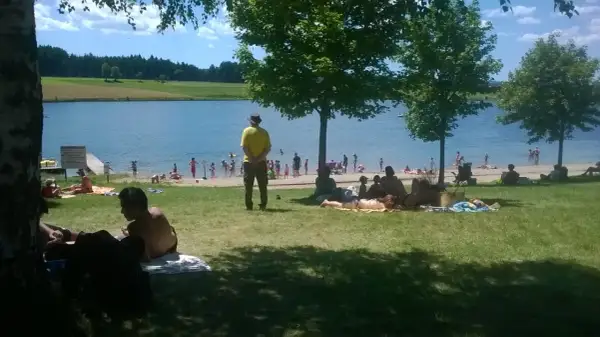 Journée ensoleillée au lac de Naussac, baigneurs et familles profitent de la plage et de l'eau.