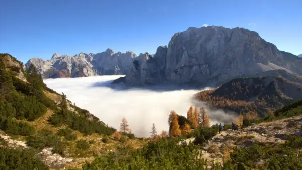 Vue spectaculaire des Alpes Juliennes, avec une mer de nuages enveloppant les vallées et des montagnes majestueuses sous un ciel bleu.