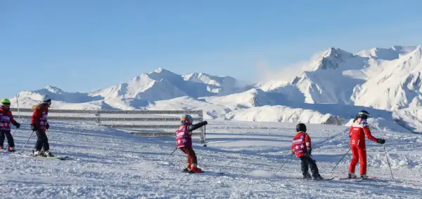 Enfants en plein cours de ski, profitant d'une journée ensoleillée avec des montagnes enneigées en arrière-plan.