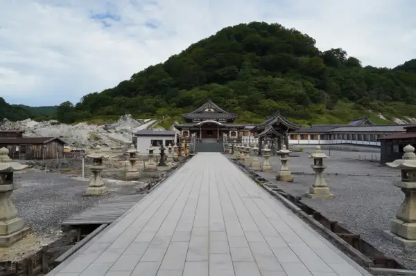 Allée de lanternes menant à un temple au pied du mont Osore, paysage volcanique et verdoyant.