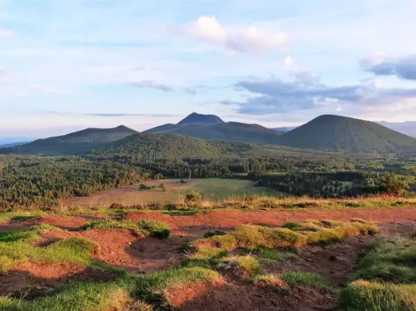 Vue panoramique sur les volcans d'Auvergne, avec le Puy Chopine dominant la forêt verdoyante sous un ciel nuageux.