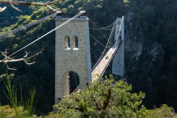 Le viaduc des Rochers Noirs, un pont suspendu impressionnant, traverse une vallée verdoyante. Deux personnes à vélo profitent de la vue.