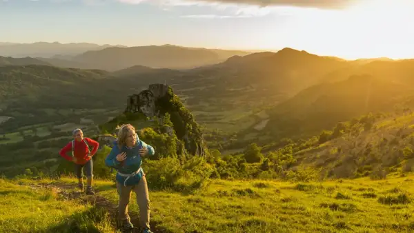 Deux randonneurs sur le sentier des cathares, profitant d'un paysage montagneux baigné par le soleil couchant.